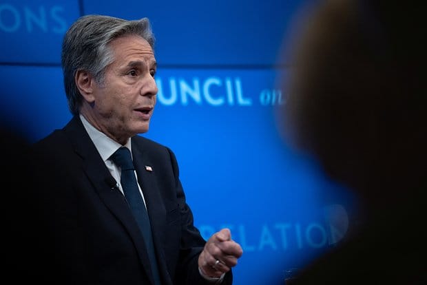 Antony Blinken discursando, com um telão azul ao fundo.